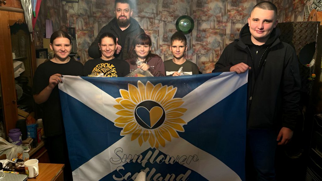 Family in Kryvyi Rih holding Scottish flag with a logo of Sunflower Scotland
